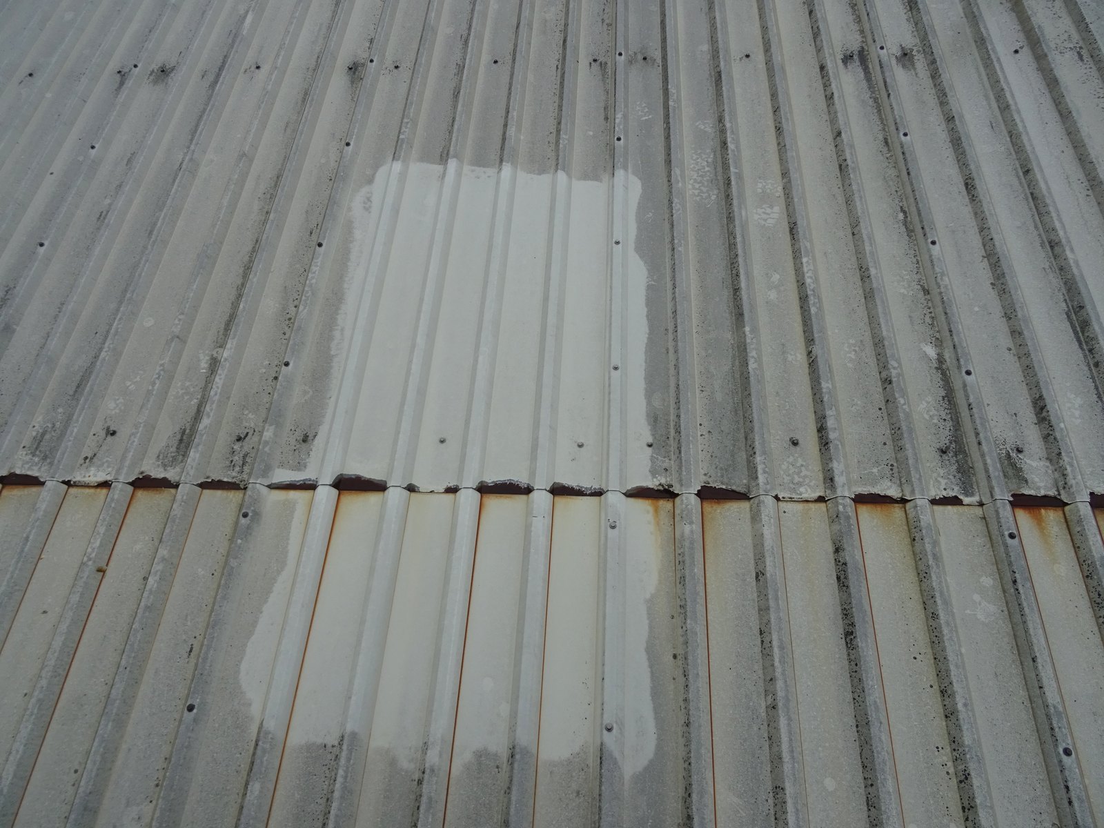 Cut-edge corrosion at the end-lap of profiled metal roof cladding, with coating breakdown and rust staining along the sheet edge.